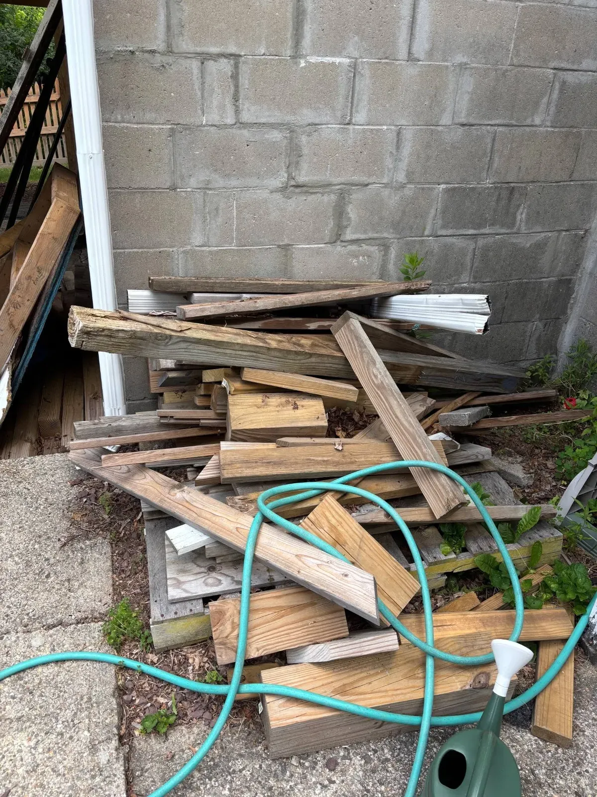 Pile of old scrap lumber and a garden hose beside a house