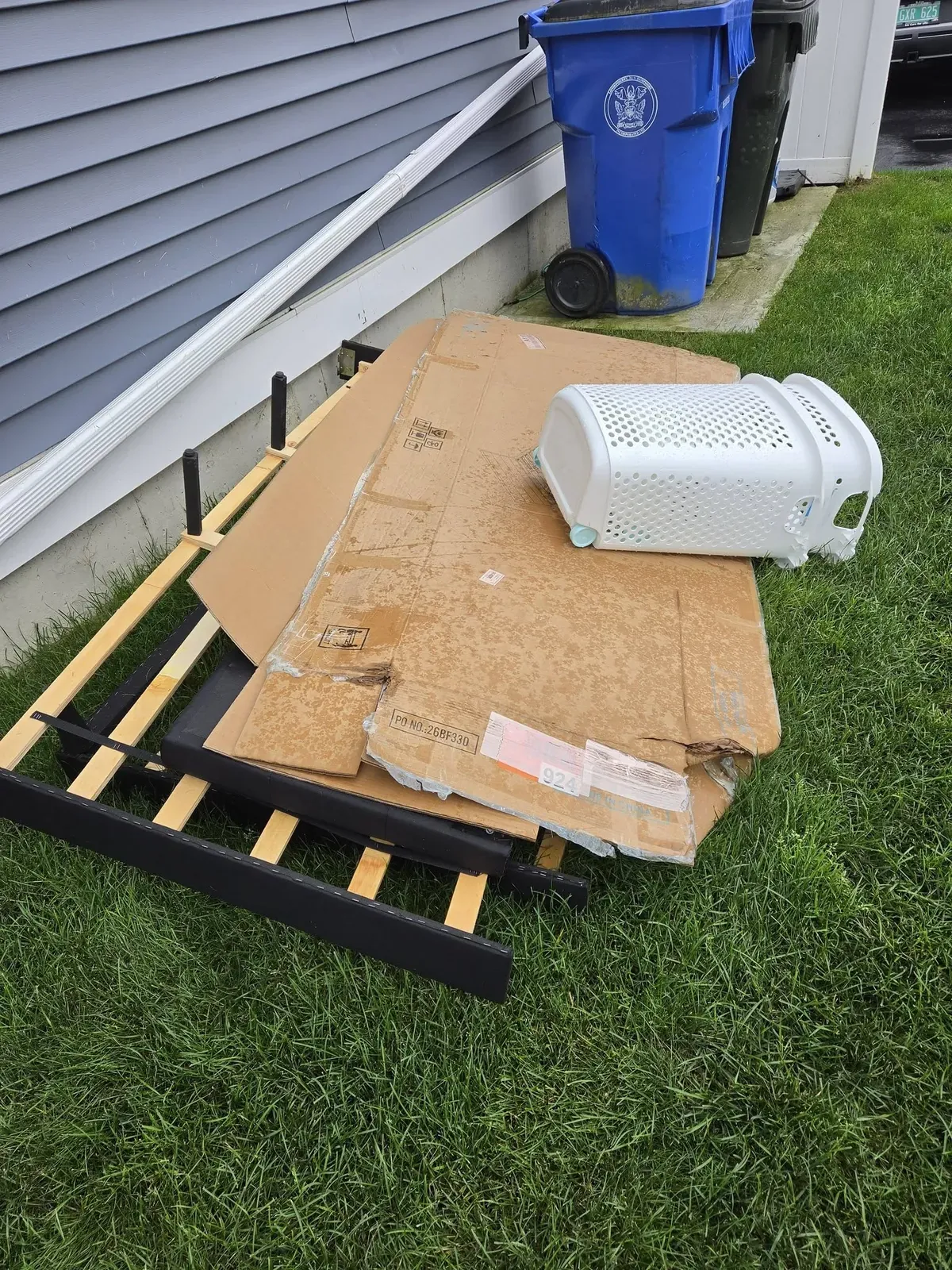 Bed frame, flattened cardboard and a laundry basket on a lawn