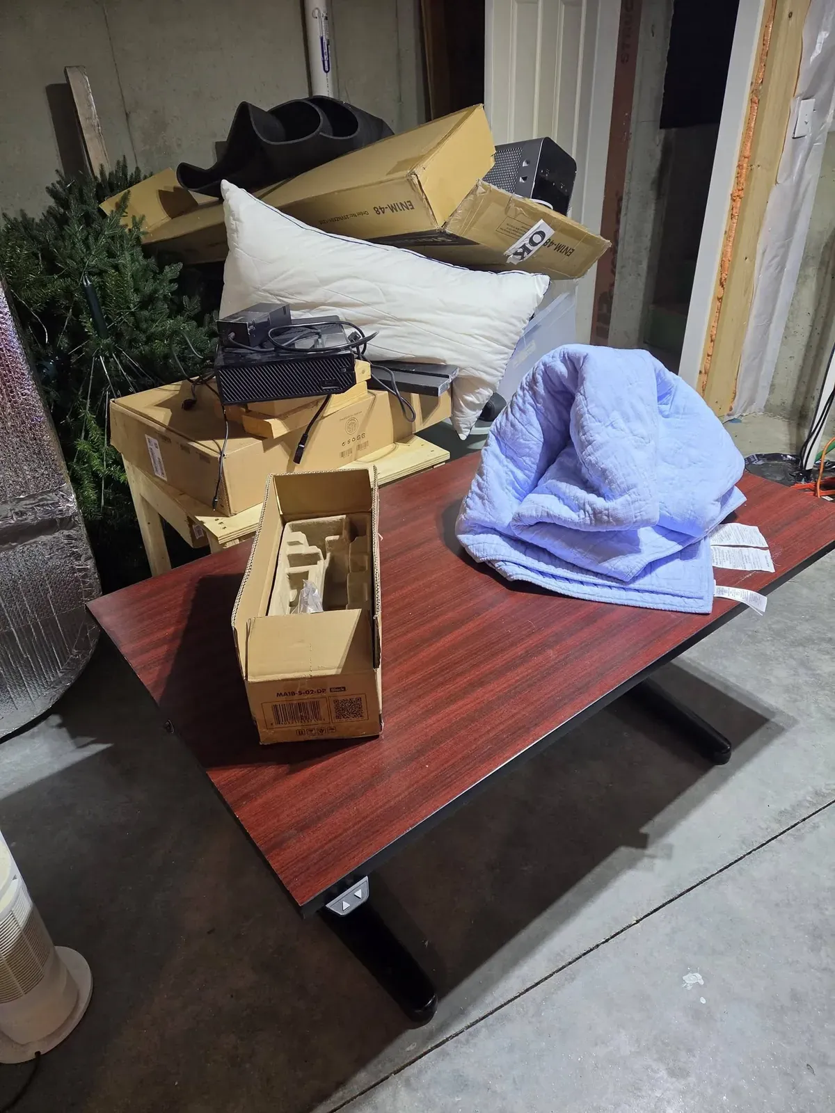 Wooden desk stacked with boxes, a pillow and a blanket in a garage