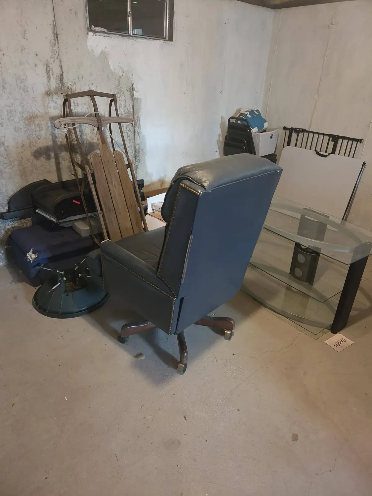 Leather office chair, glass TV stand and an old sled in a basement