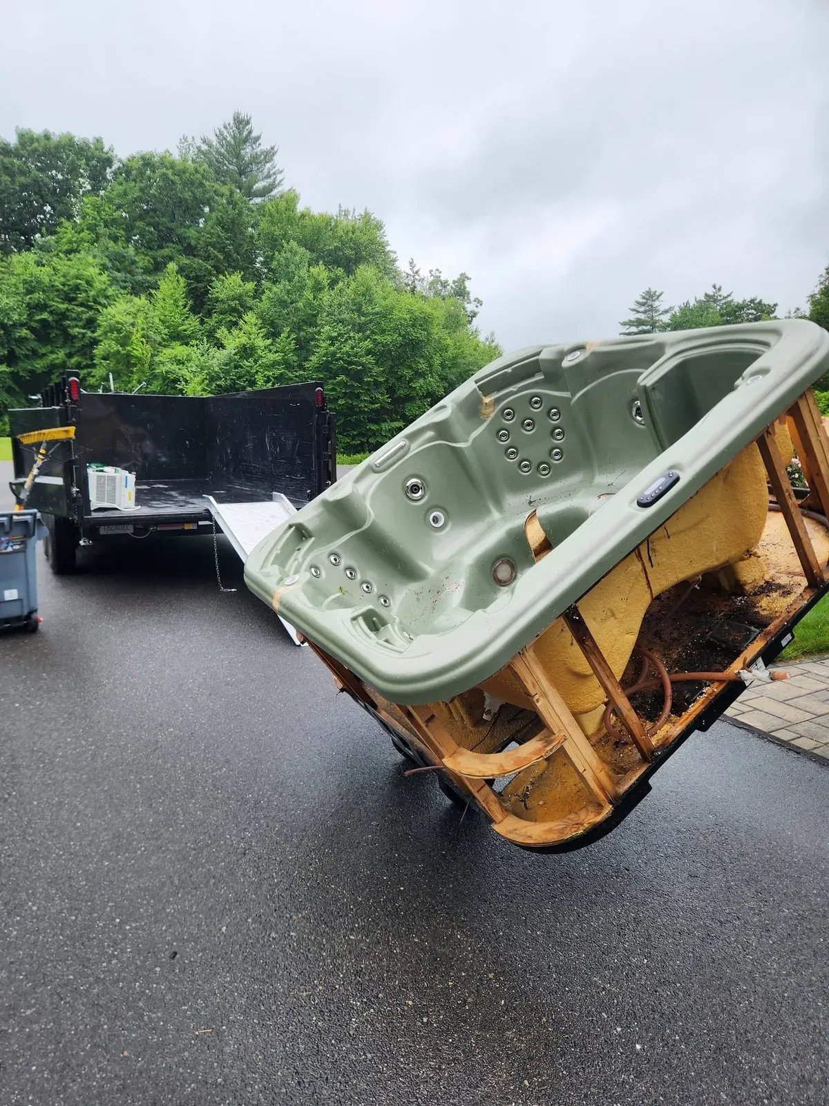 Old hot tub tipped on its side in a driveway on its way to the trailer