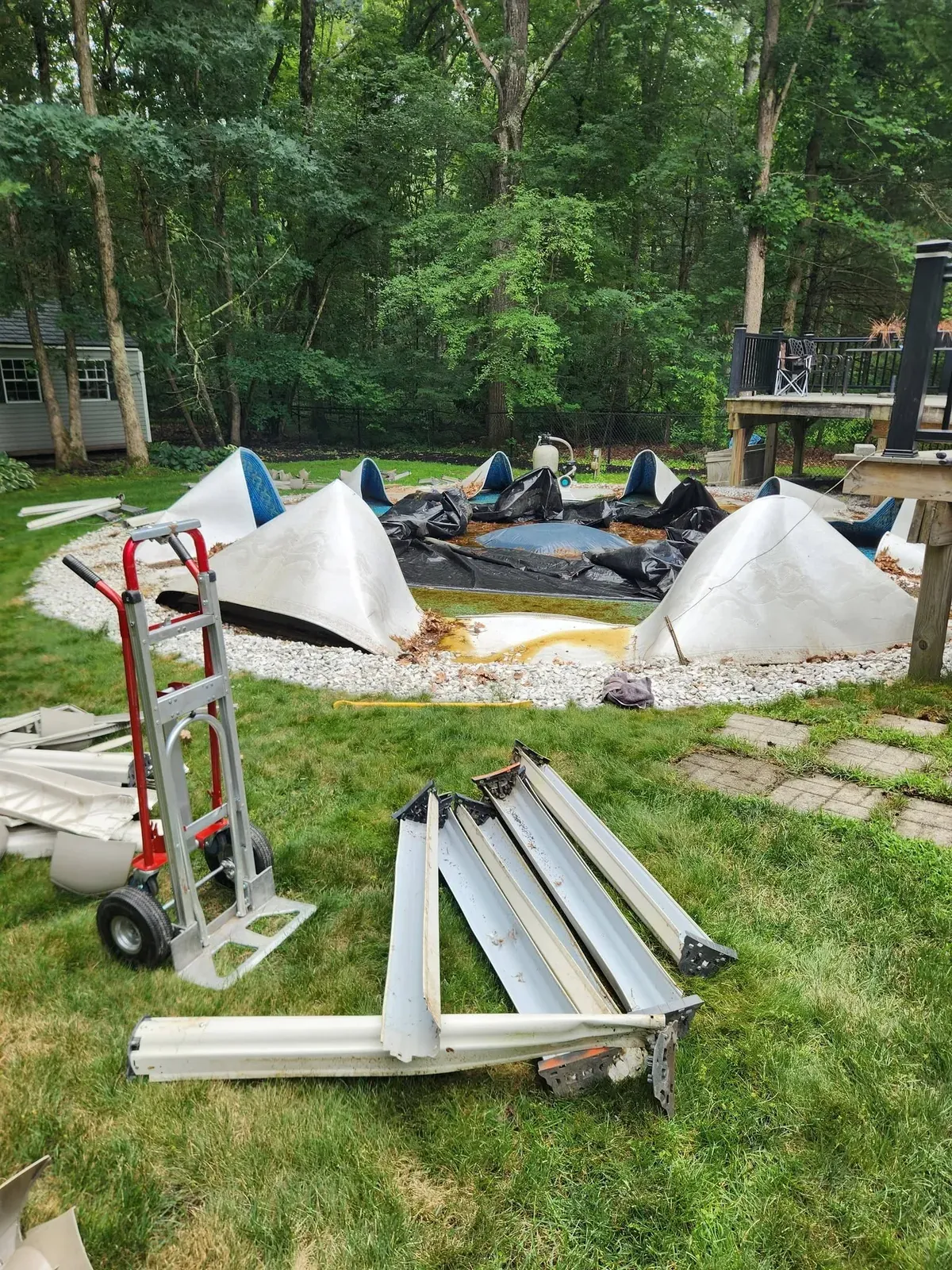 Above-ground pool walls broken down, with panels and a hand truck on the lawn