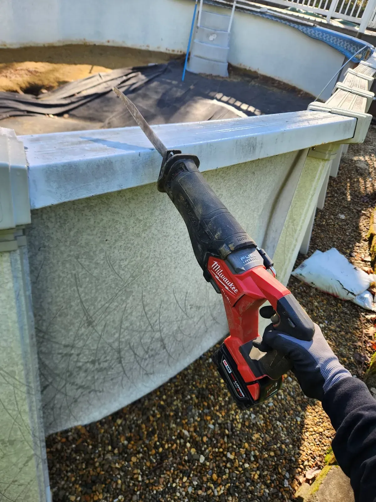 Crew member cutting through an above-ground pool wall with a reciprocating saw
