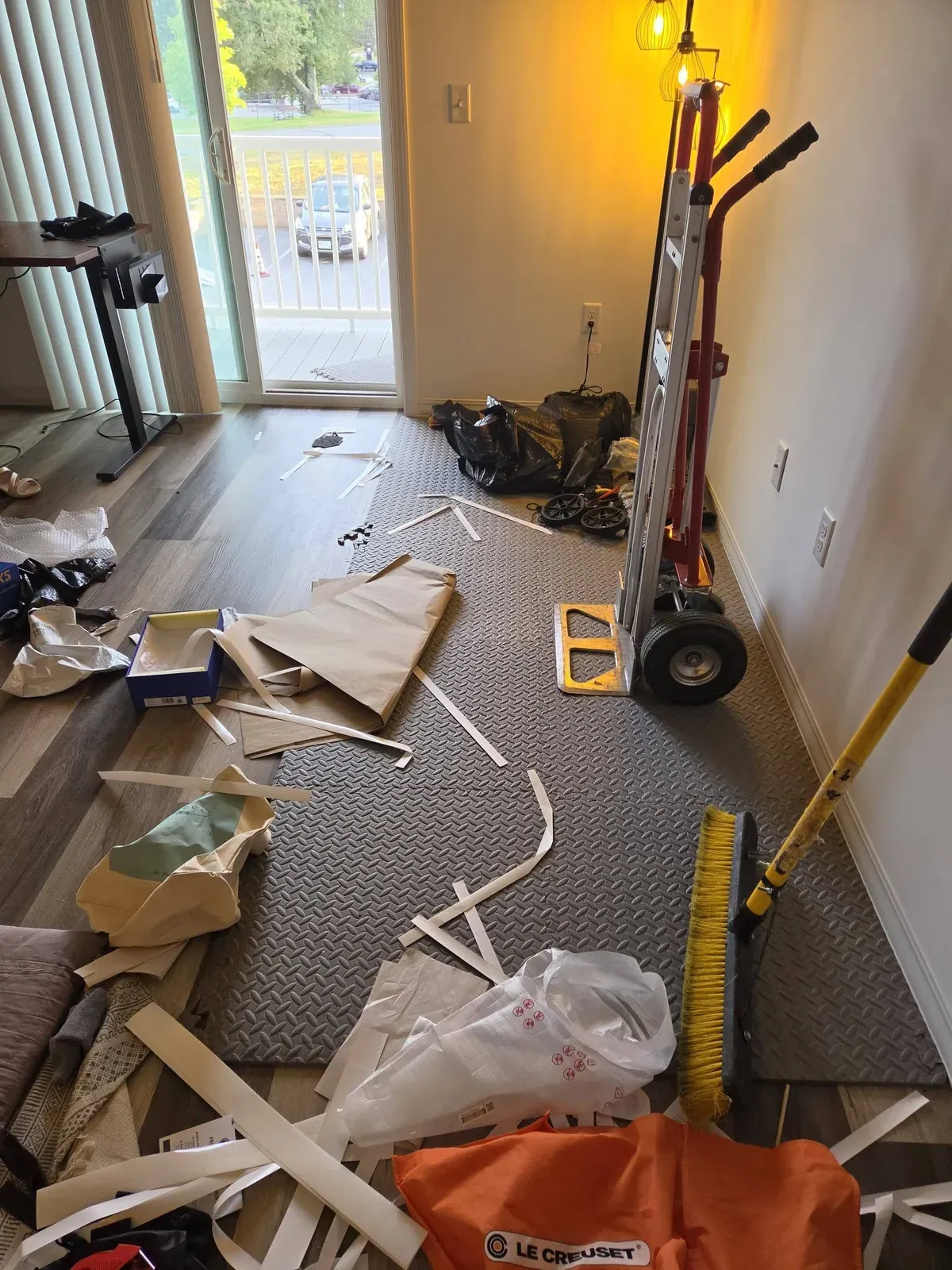Apartment floor covered with packing debris, with a hand truck and broom