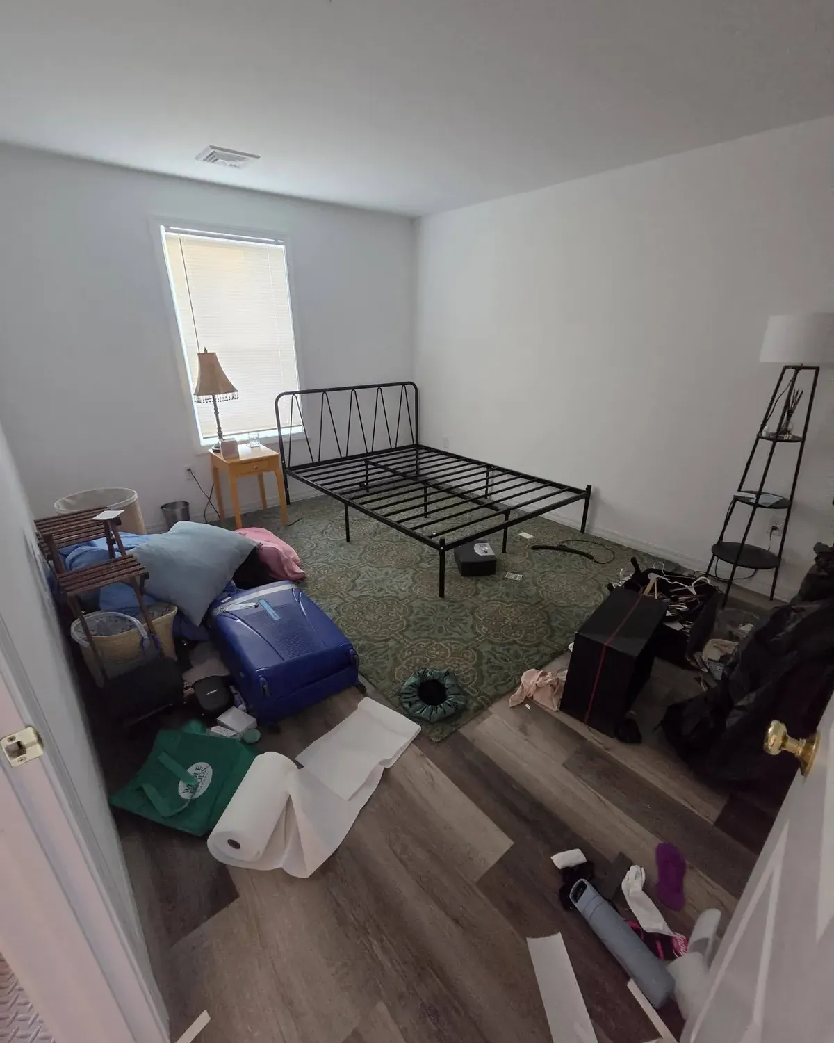 Bedroom left with a metal bed frame, luggage and scattered items