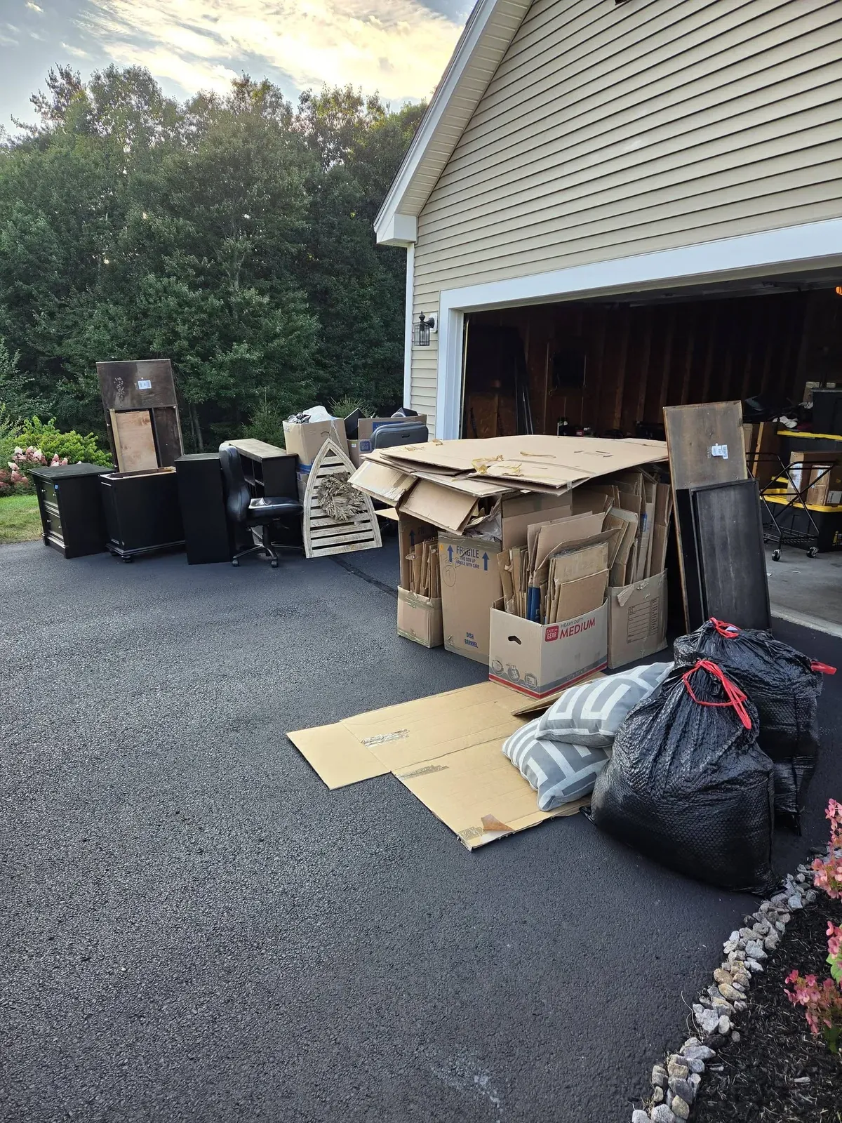 Flattened boxes, furniture and trash bags in a driveway outside a garage