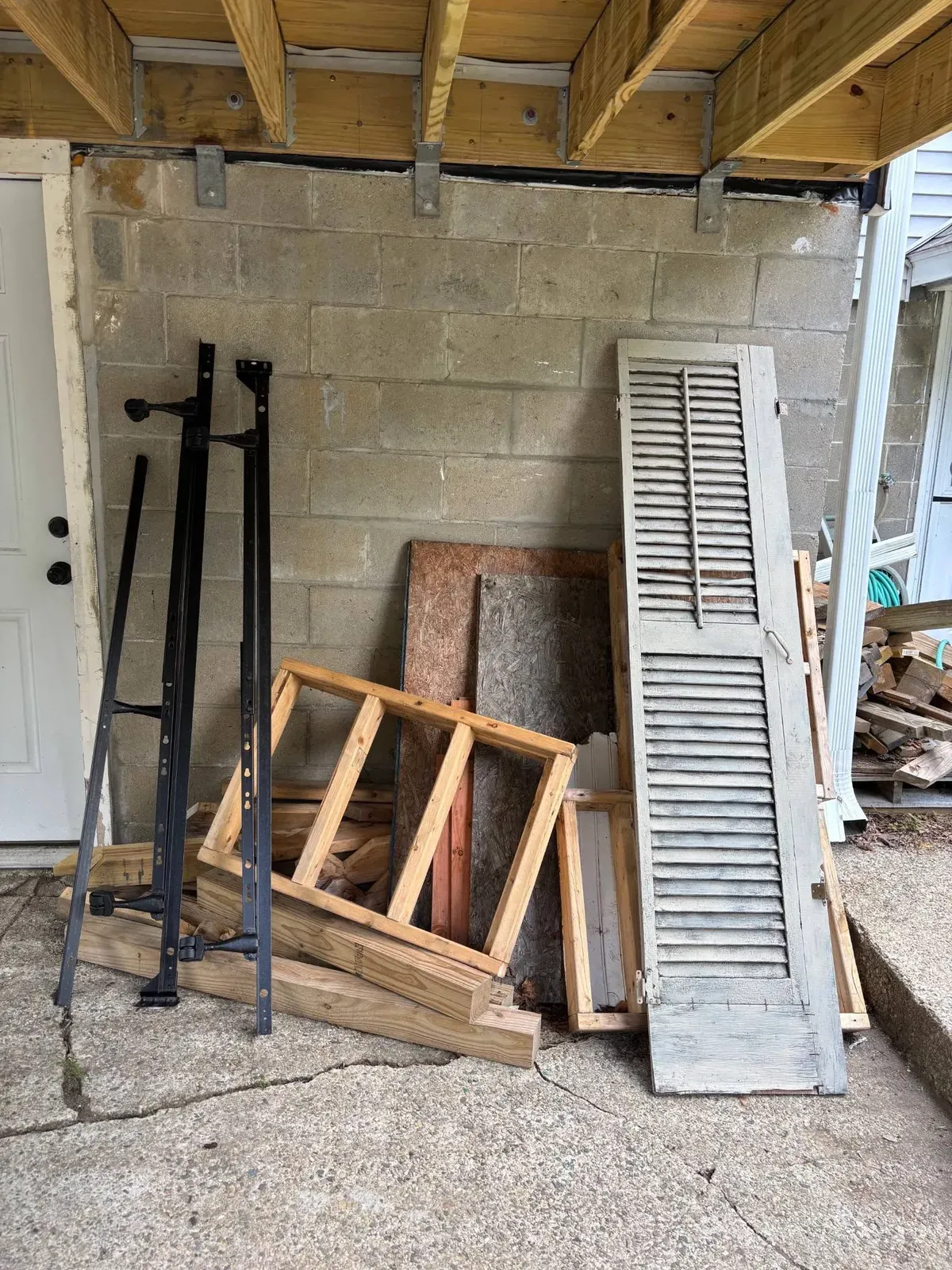Metal bed rails, a wooden shutter and scrap wood leaning against a wall