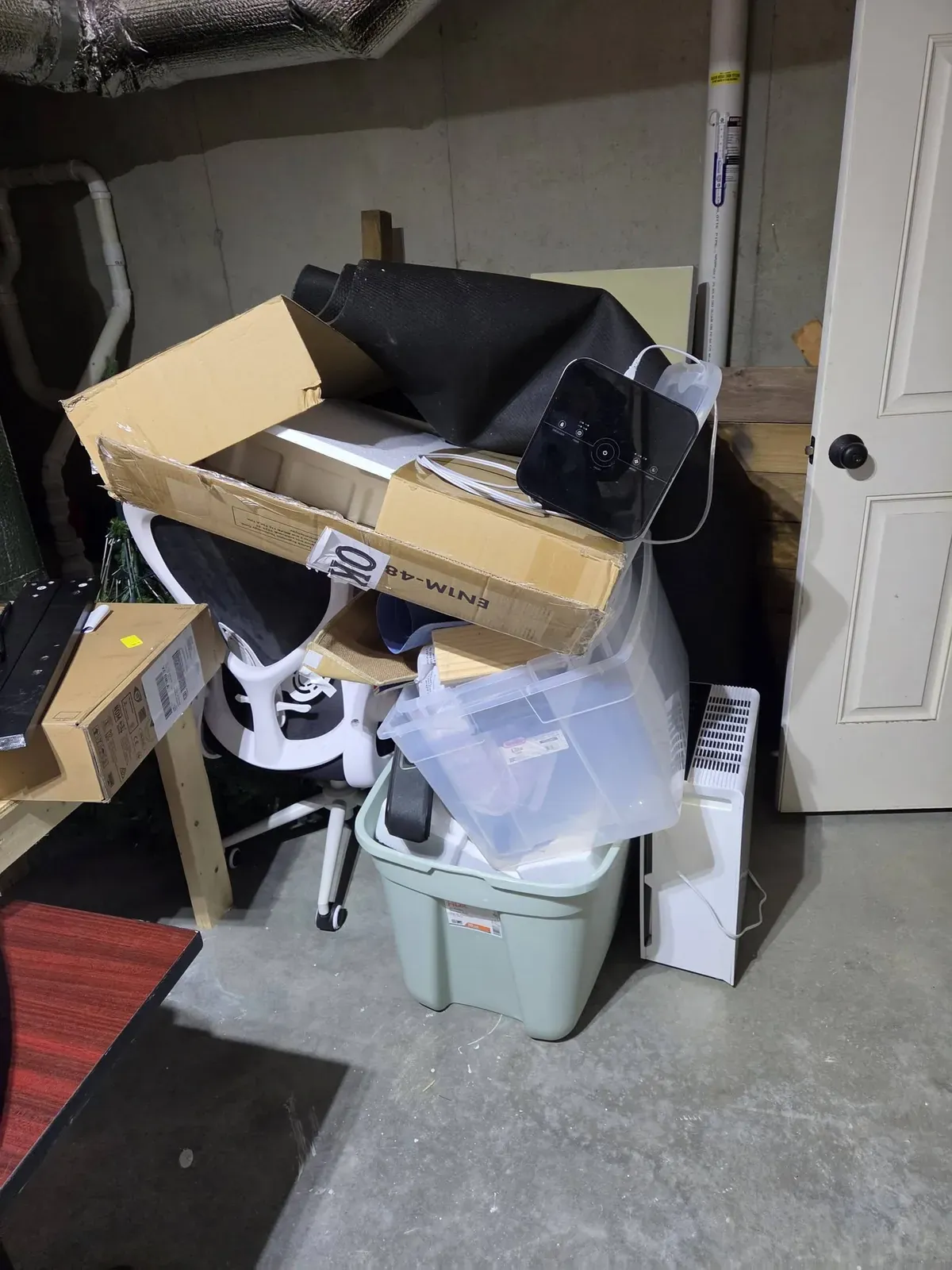 Boxes, a fan, storage bins and an office chair piled in a garage corner