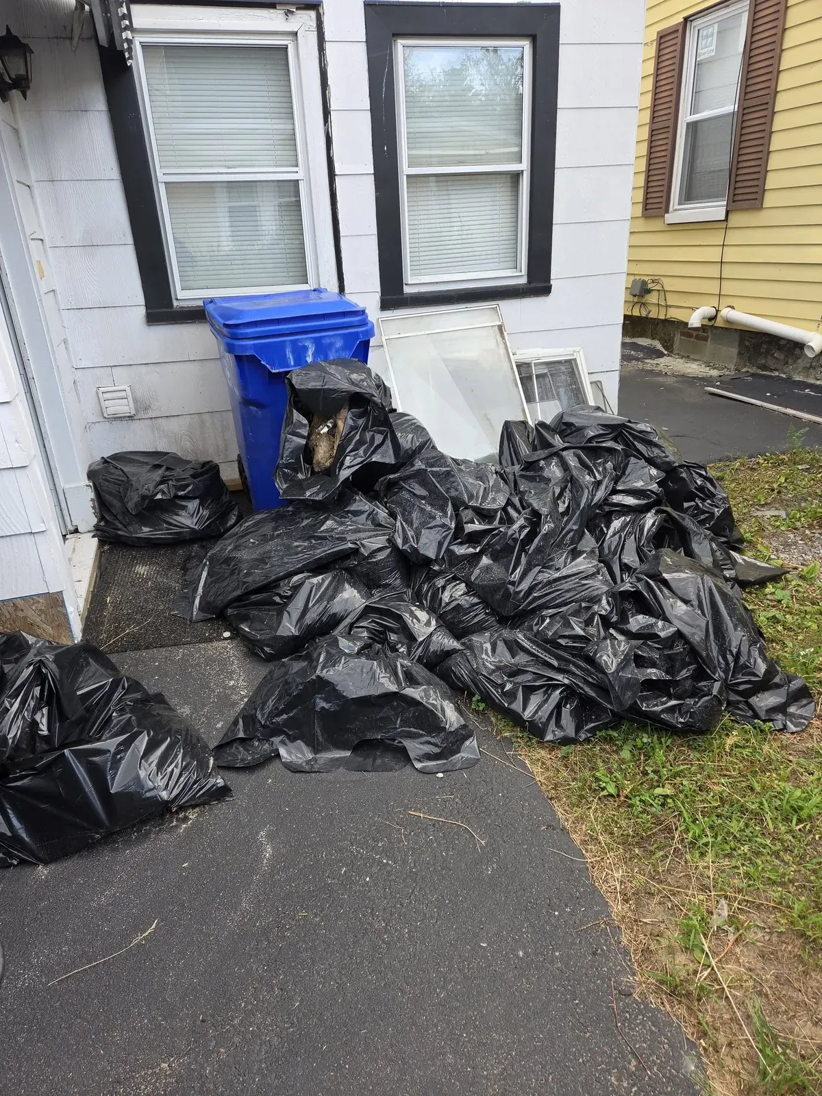 Pile of black trash bags and old windows beside a house