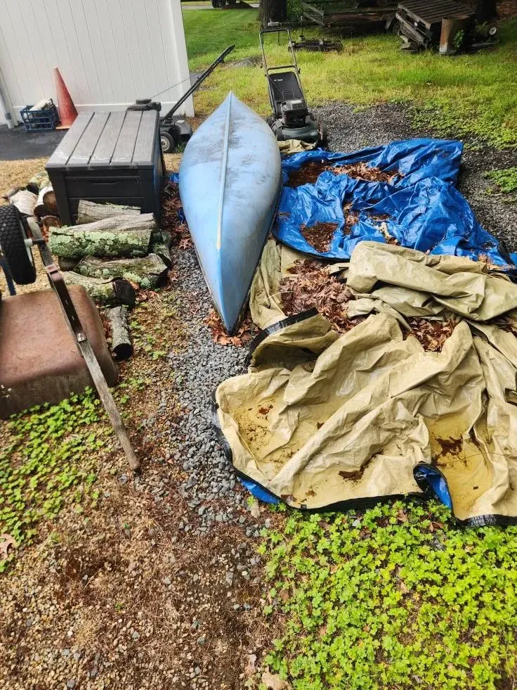 Old lawn mower, kayak, tarps and yard items piled beside a shed